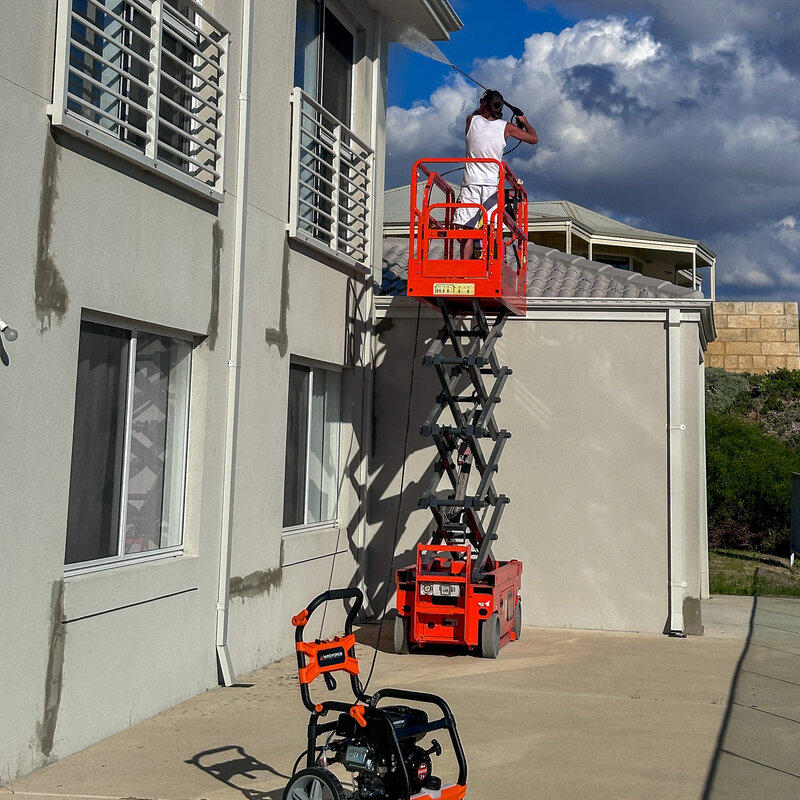 Handyman pressure washing exterior of two-story house off a scissor lift.