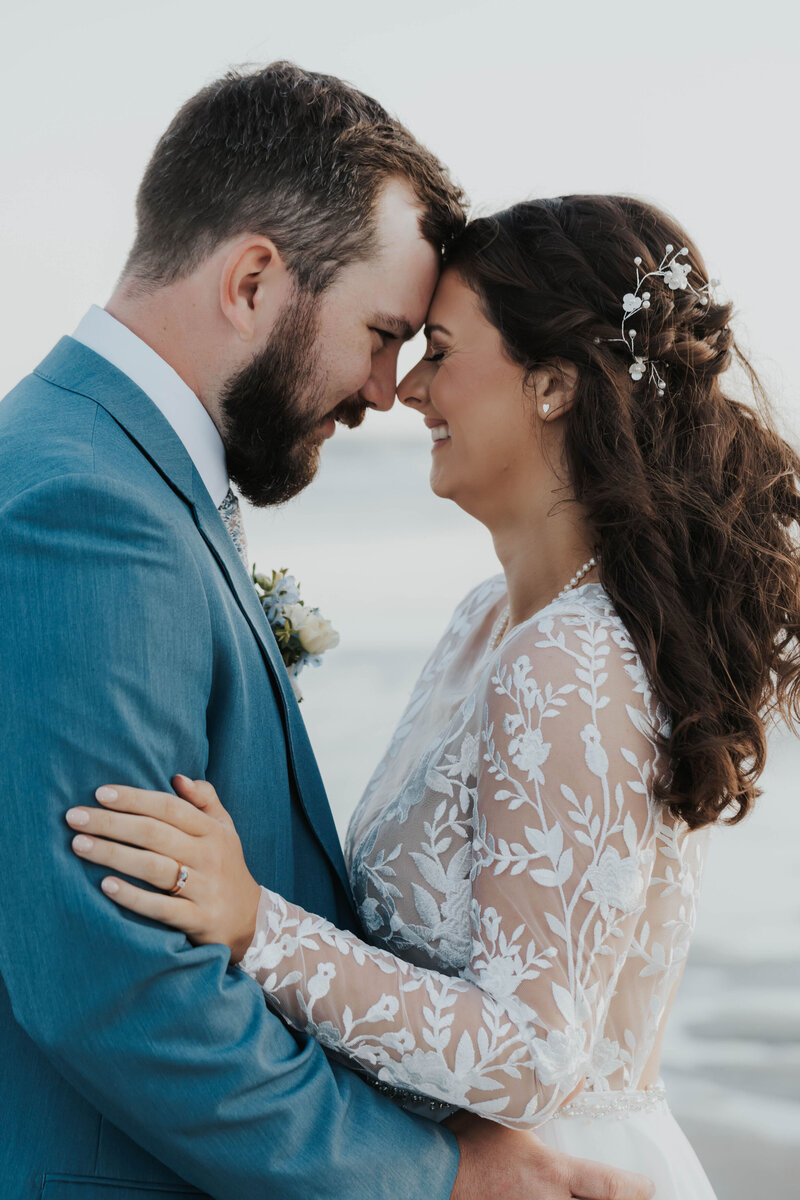 bride and groom touching foreheads on beach