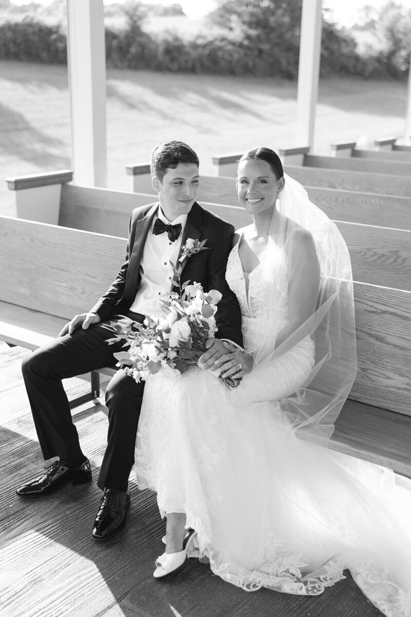 Black and white image of bride and groom sitting on pews at Nashville wedding