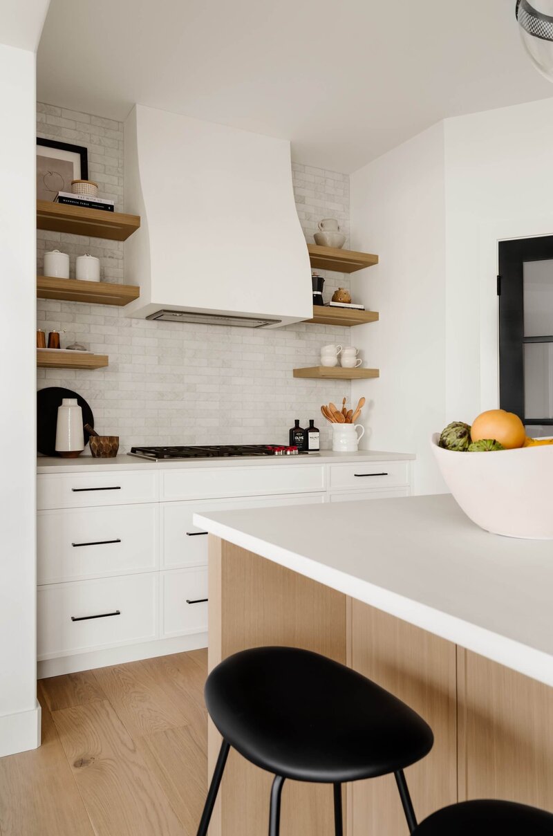 A modern farmhouse kitchen with plaster hoodfan, white oak open shelving and black accents paired with subway tile. 