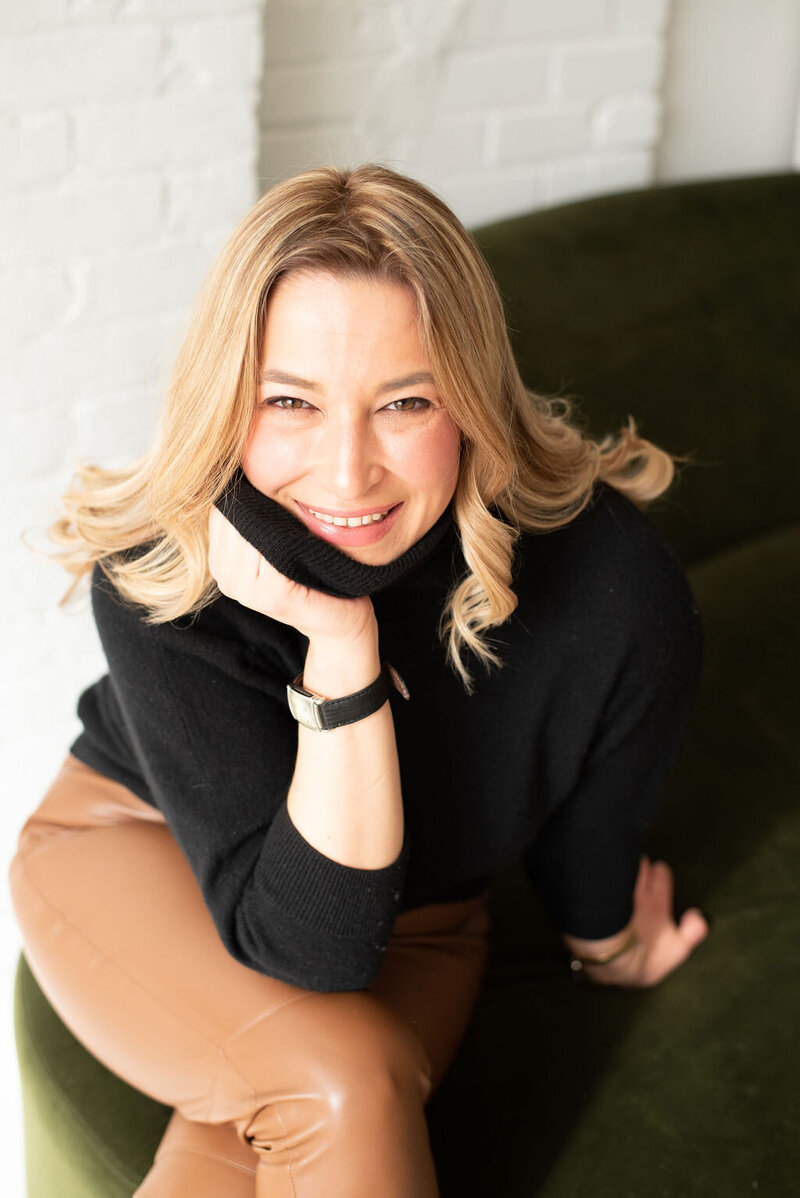 The copywriter Laura Gatsos Young, smling and seated on a green ottoman