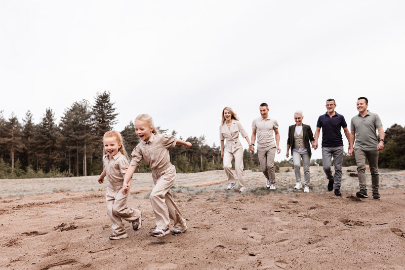Familie rent in de bossen in Sevenum naar de fotograaf met de twee kleinkinderen in beige pakjes voorop