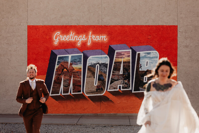 Eloping couple stands with Moab welcome painted mural