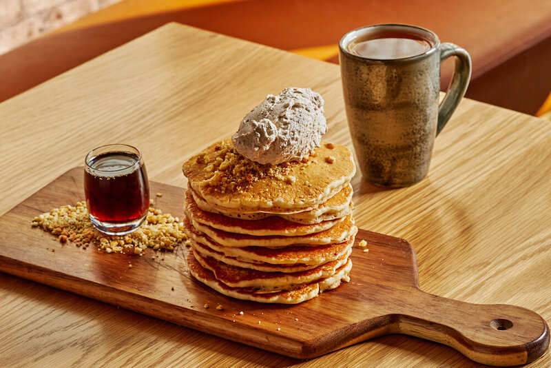 Freshly stacked pancakes with a side of maple syrup and a cup of coffee