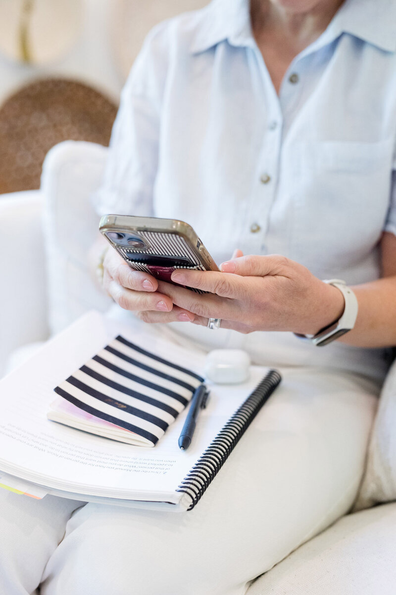 Dinah sitting with a notebook on her lap and her phone in her hand