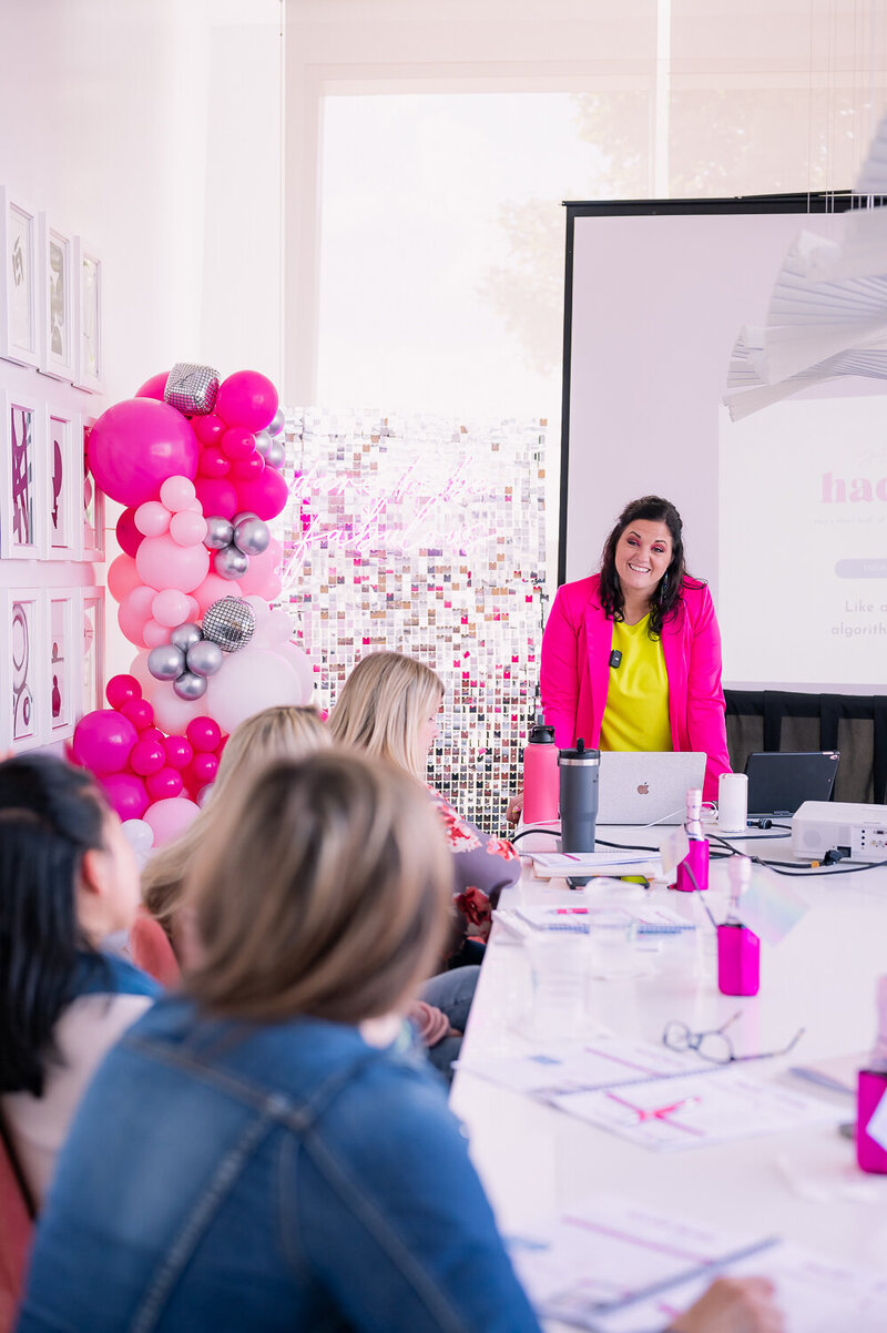 Jessi Cabanin holding a pink planner notebook sitting at a desk with a laptop and boss babe coffee cup on it.