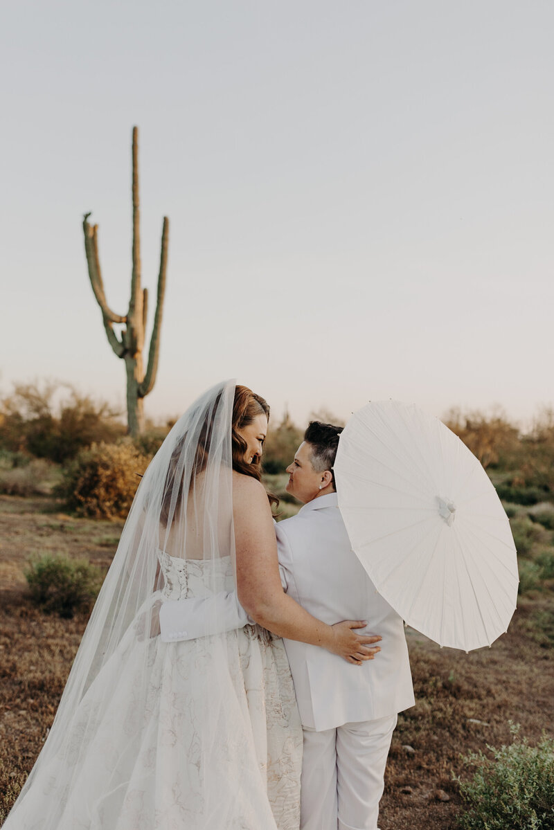 two brides hug with parasol in the desert