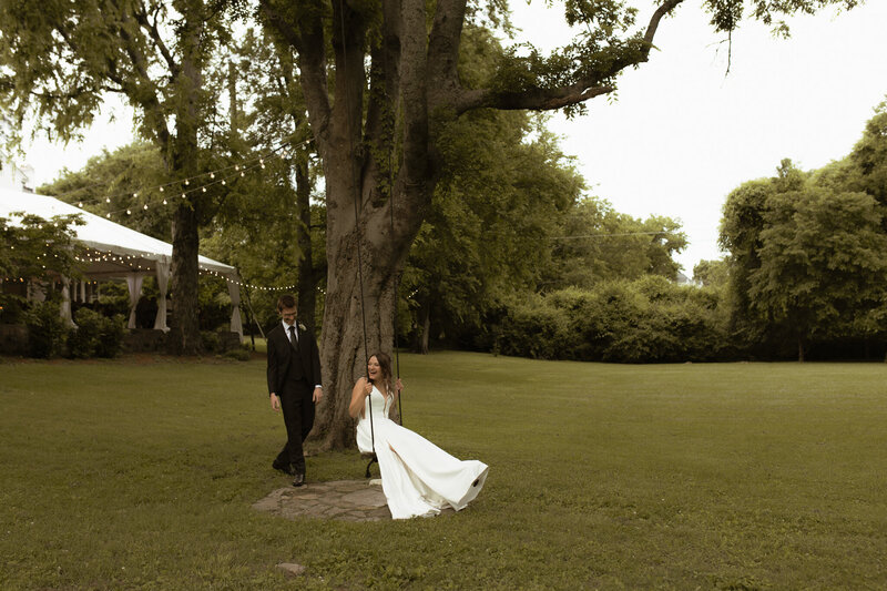 wedding photo shot of bride and groom where groom is pushing bride smiling on a swing