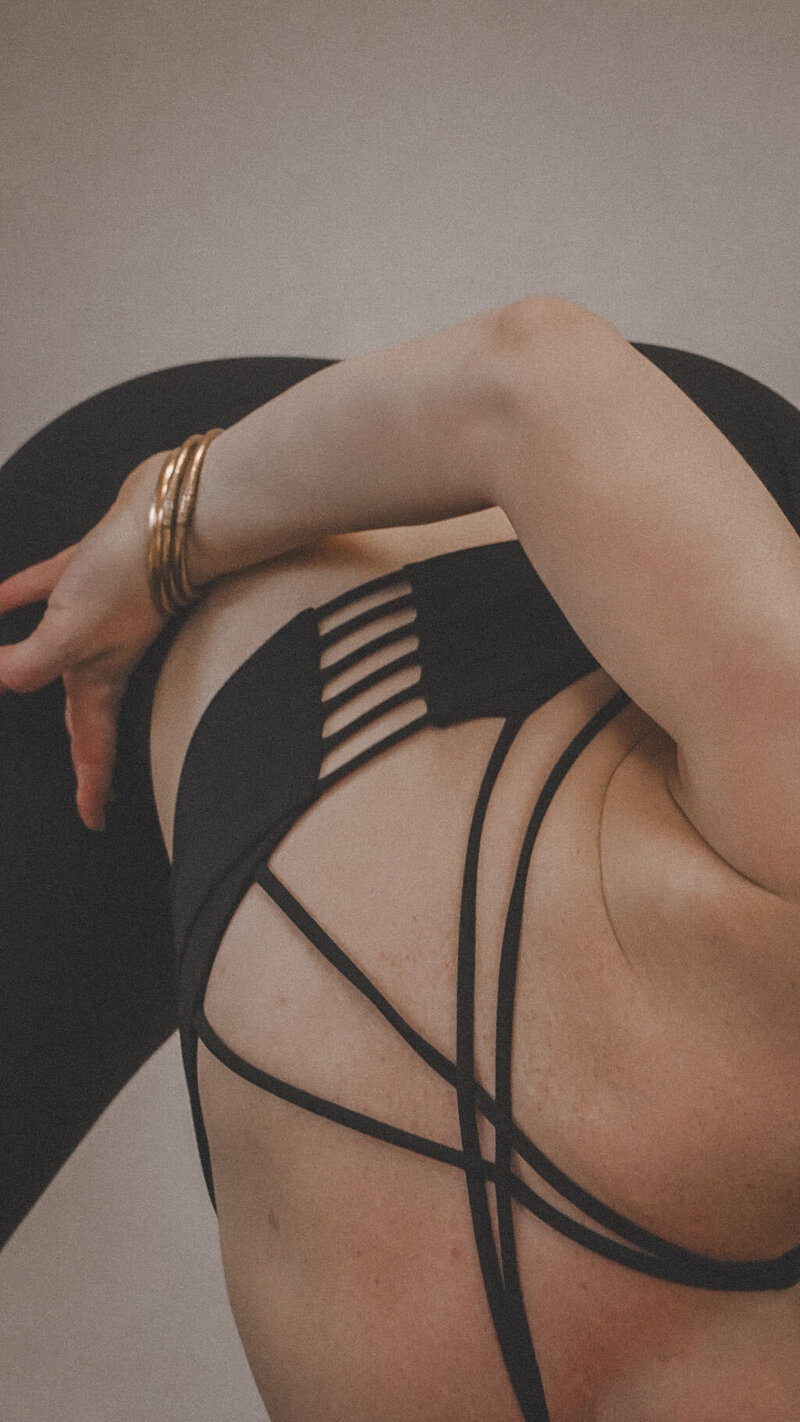 A woman in a black two-piece yoga outfit, bending over in a pose with her arm behind her back, wearing gold bangles, radiating grace and focus.