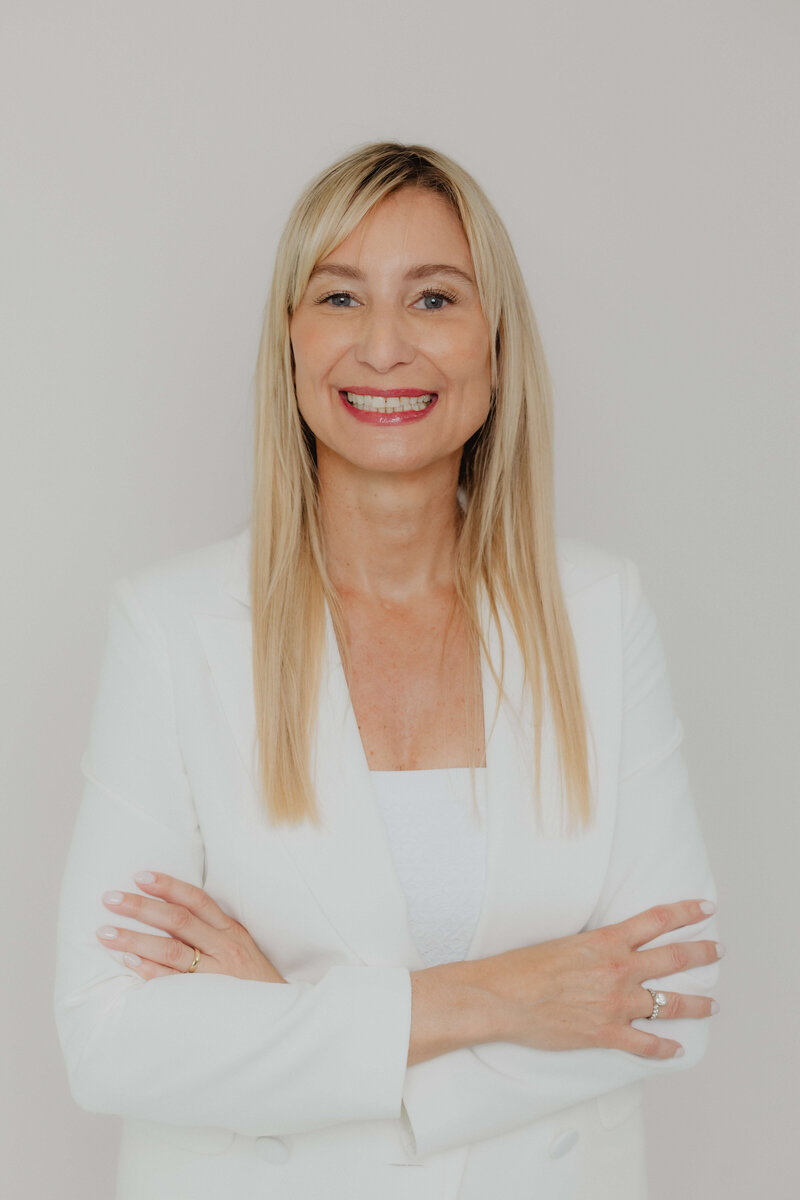 Close of a blonde women smiling in a white suite.