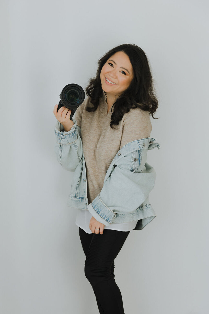 Asian woman holding camera in jean jacket