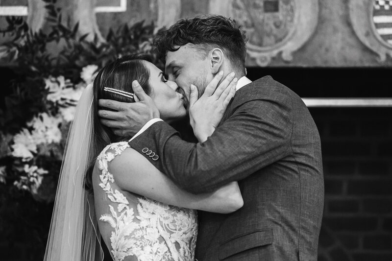 Een intiem zwart-wit moment van een bruid en bruidegom die elkaar liefdevol omhelzen tijdens hun trouwceremonie.