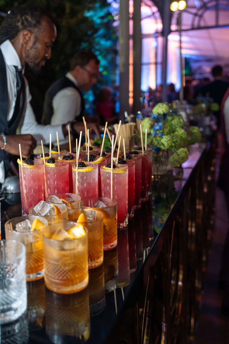 luxury party cocktail bar with rows of drinks displayed along the top of the bar and two mixologists making drinks behind it
