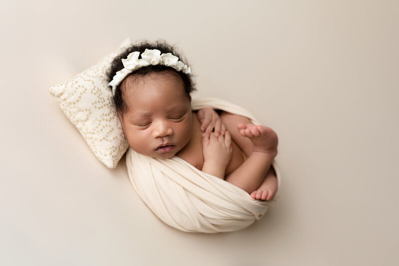 sleeping newborn baby with headband posed on creamy blanket