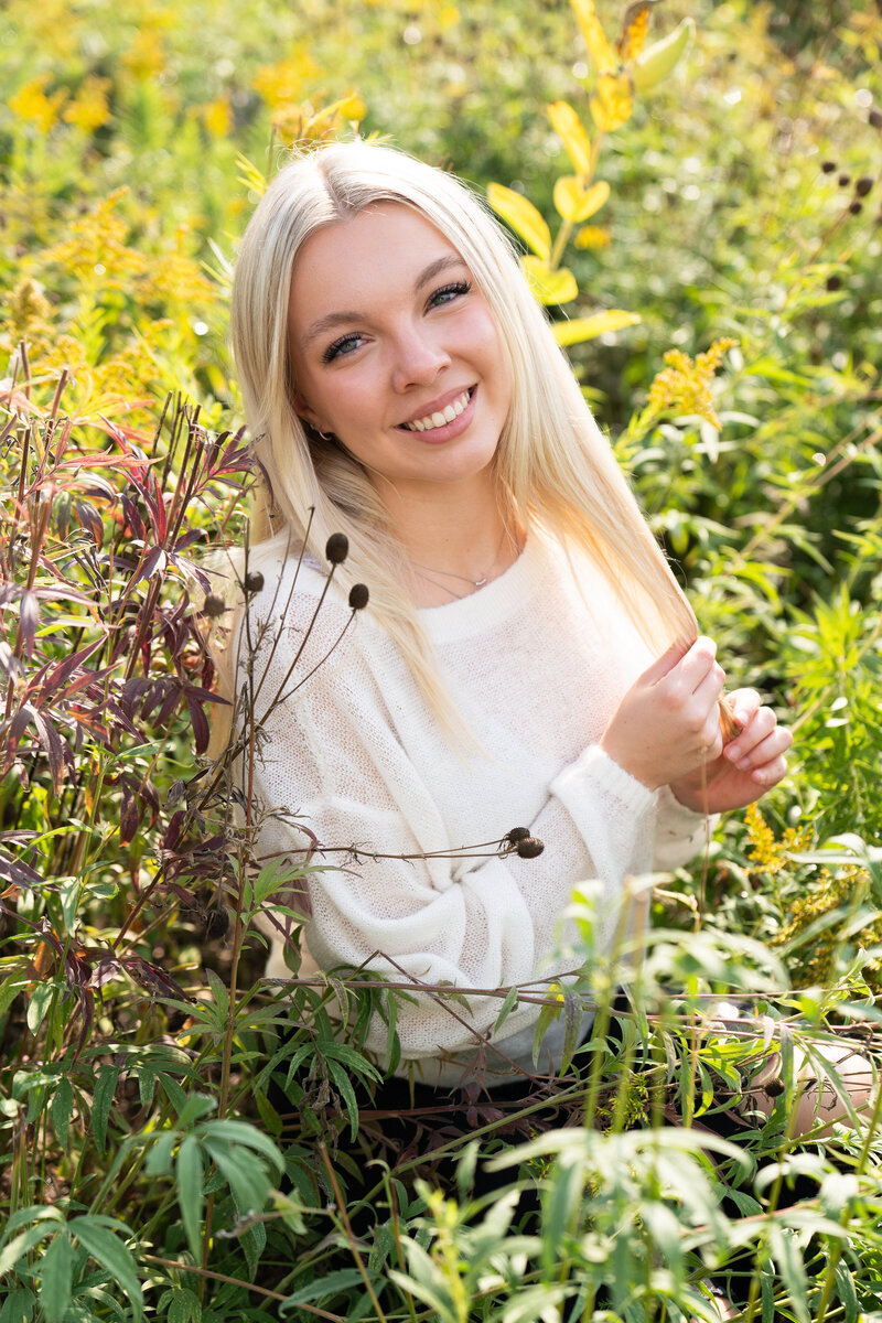 High school girl sits in a wildflower field for her senior photos