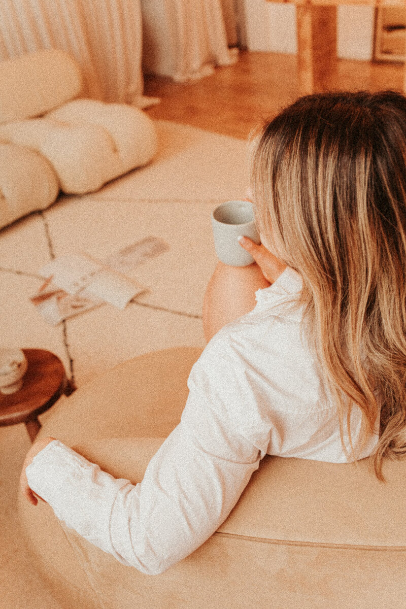 Girl sitting on a couch, drinking coffee. Her back is turned to the camera.