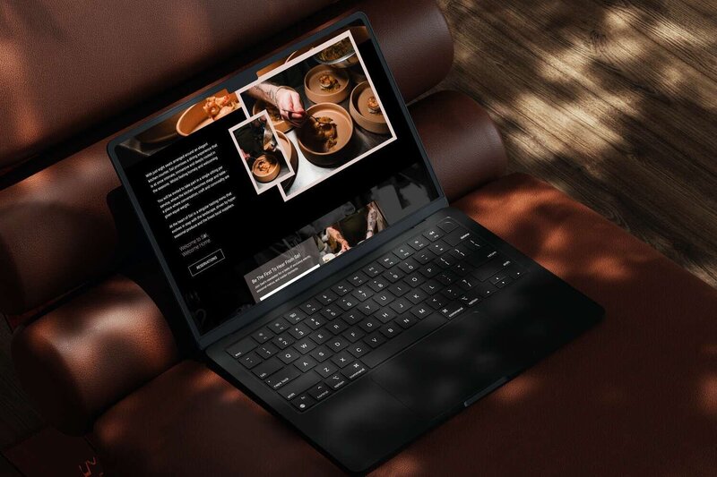 Black laptop on a brown leather seat showing a fine dining premium restaurant website with plated food photos and a tattooed chef preparing dishes.