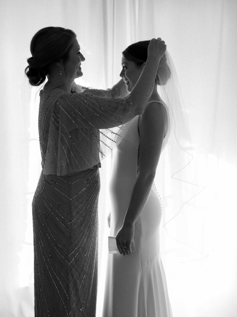 Black and white photo of mom helping bride put on her veil