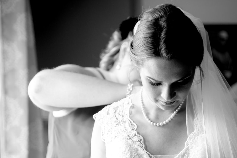 A bride gets her dress buttoned by a bridesmaid.