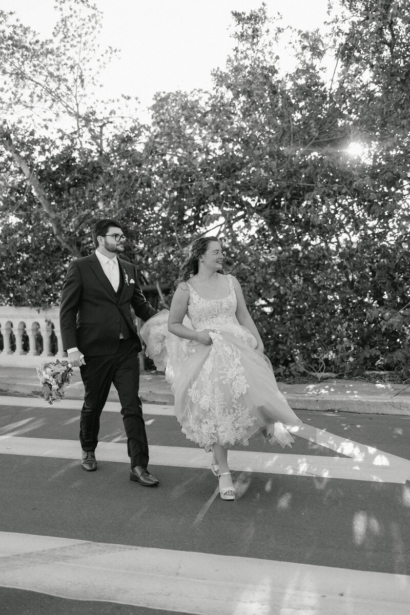Bride and groom running away together after their Sarasota courthouse wedding. The couple is walking in the street while the groom holds the bride's dress.