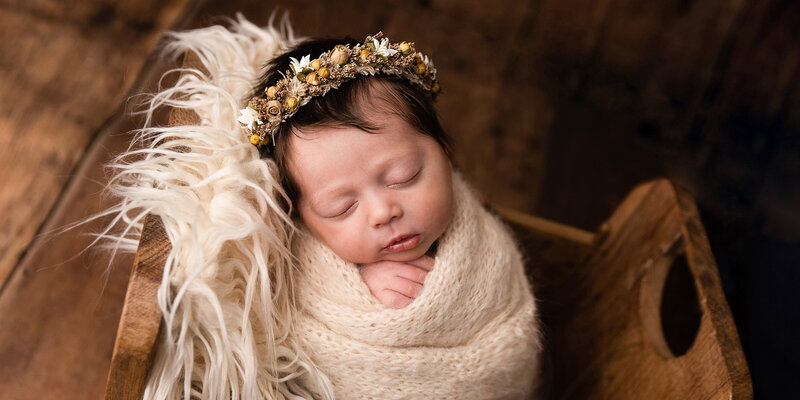 Bab y girl sleeping in wooden bed with cream wrap and flower halo.