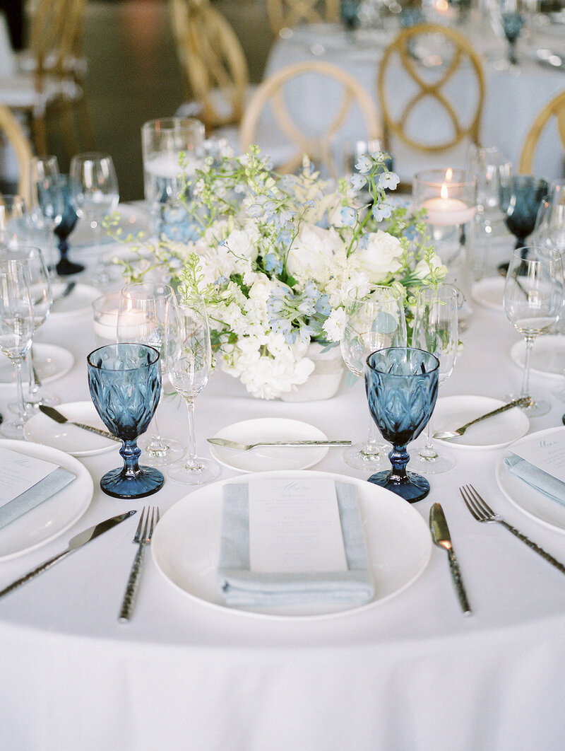 A beautifully decorated wedding reception table with blue and white flowers and glasses.