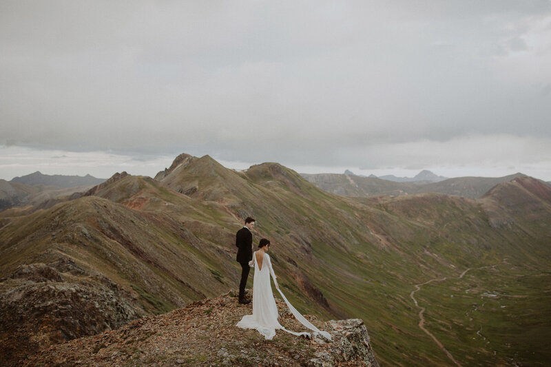 Couple stands on mountain overlook in wedding attire