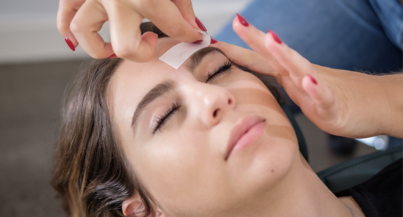 woman is receiving a brow wax with brow strips
