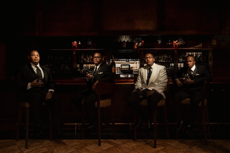 Groom and groomsmen in tuxedos at the Omni Hotel bar in downtown Indianapolis holding glasses of bourbon during wedding portrait session

