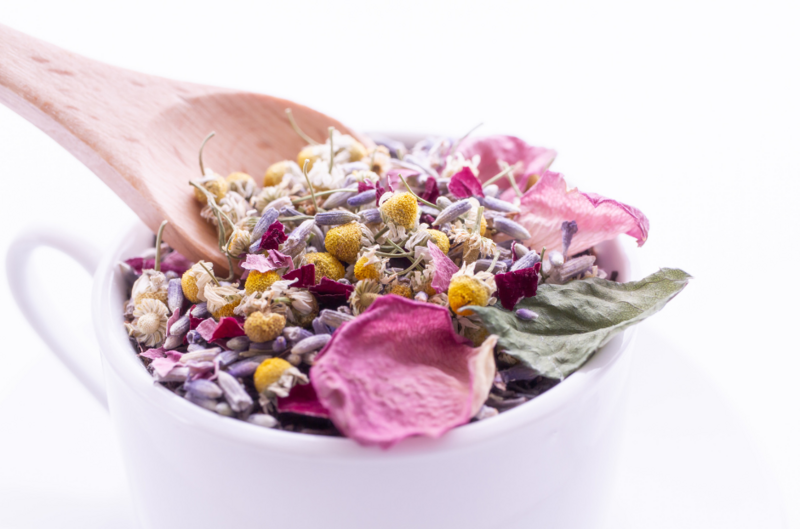 white cup filled with dried petals and herbs that support detox with wooden spoon