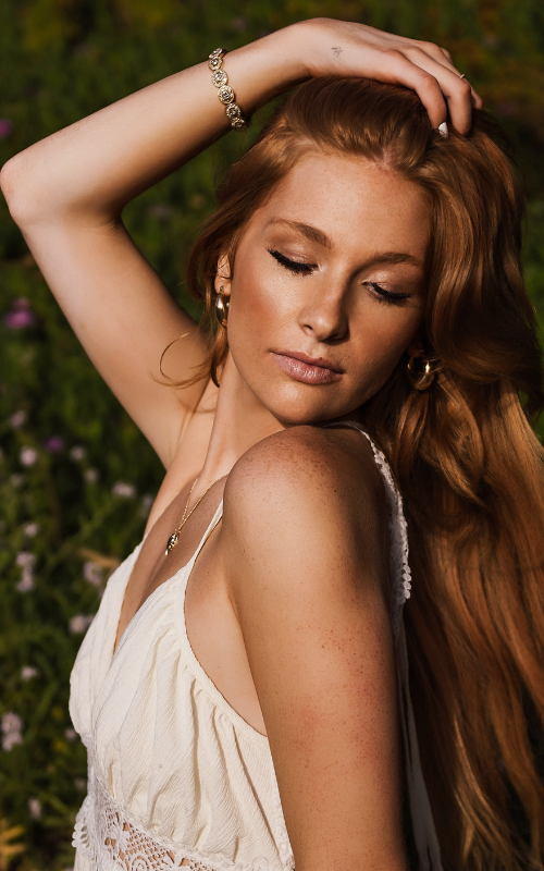 high school senior girl with long red hair and freckles looking down at her shoulder with a soft natural look