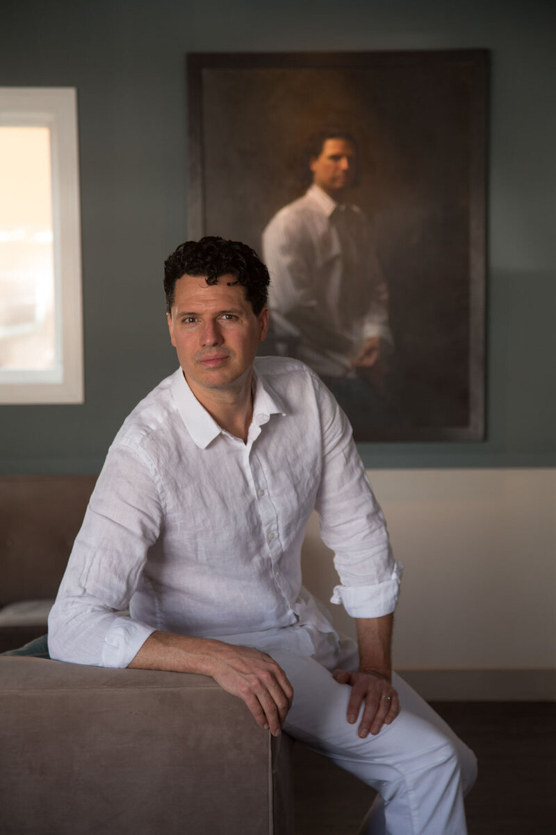 A man in a white shirt is sitting in front of a painting