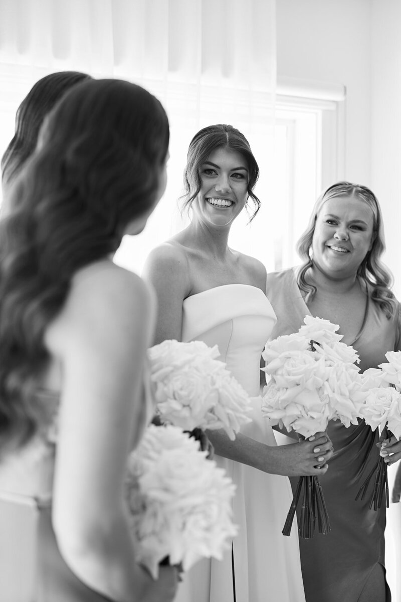 Bride looking at bridesmaids, all holding bouquets of long stemmed white reflexed roses