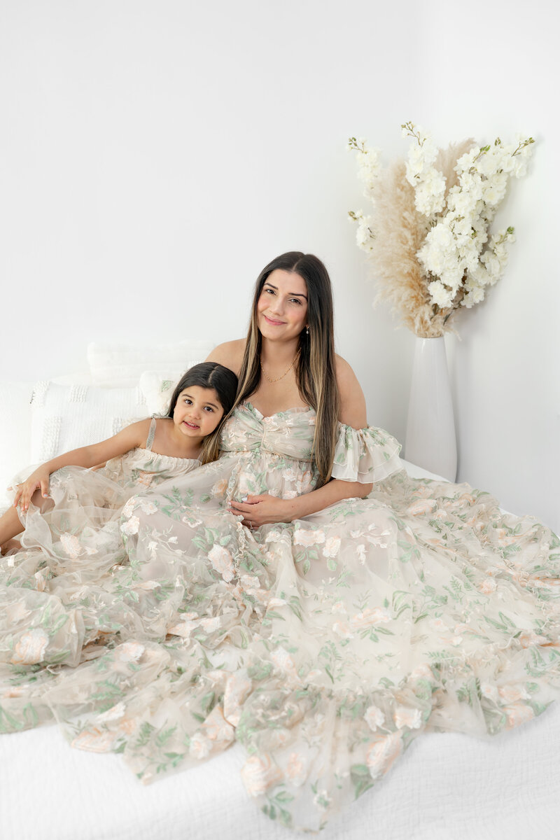 Mom cuddling daughter while one hand holds pregnant stomach