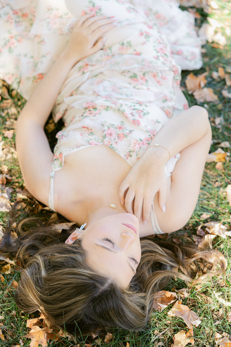 senior girl lies by leaves in floral dress during Indianapolis senior photos