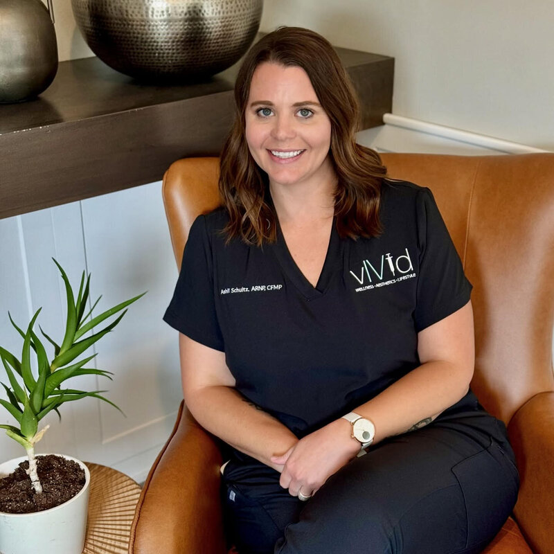 Amanda smiling, sitting in a chair at vIVid wearing black scrubs