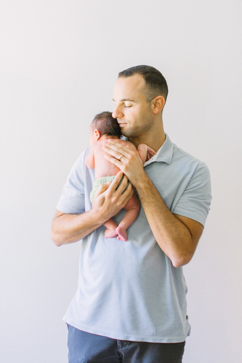 A dad in a blue shirt holds his newborn baby in a Camarillo portrait studio
