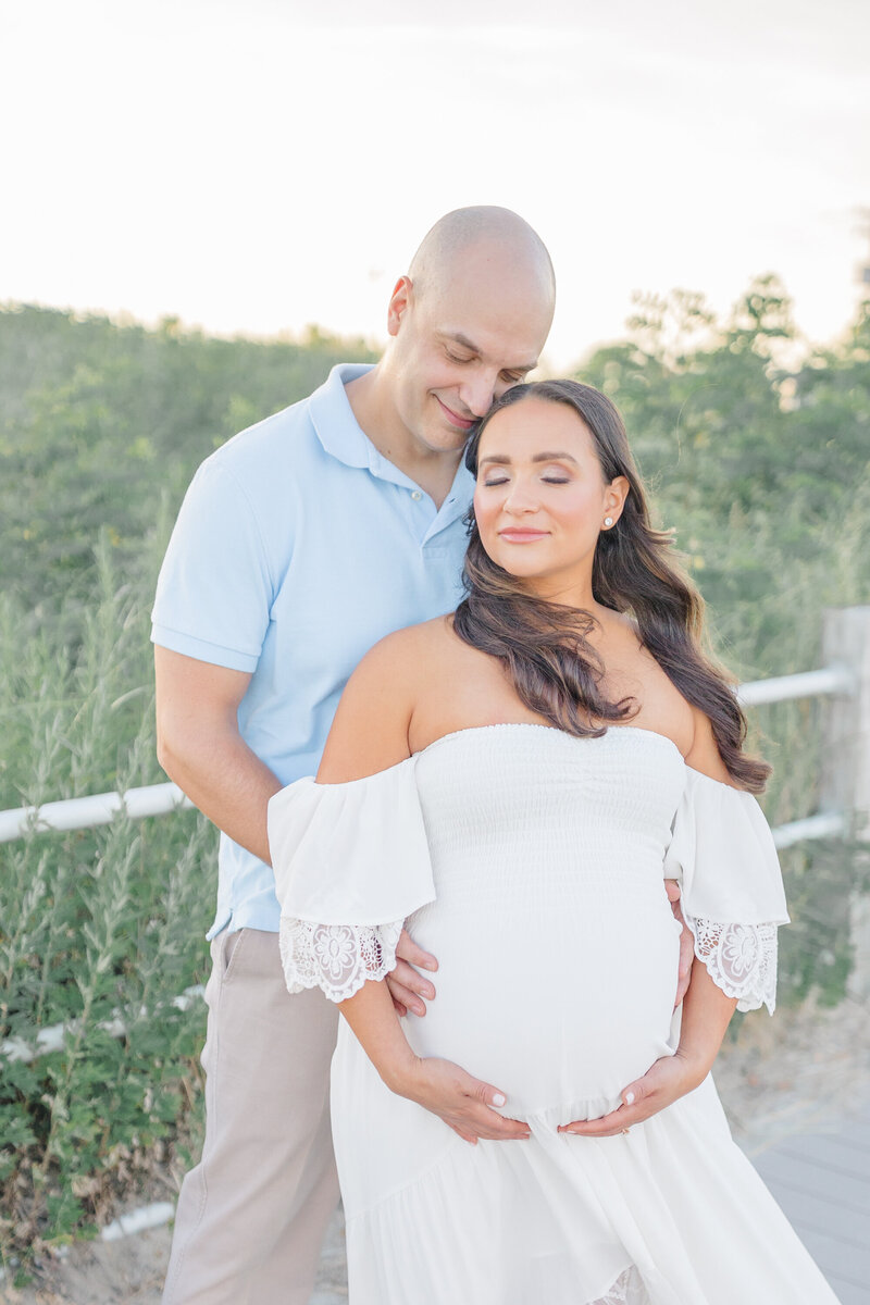 A father rests his forehead against his partner’s, their hands resting protectively over the new life they created