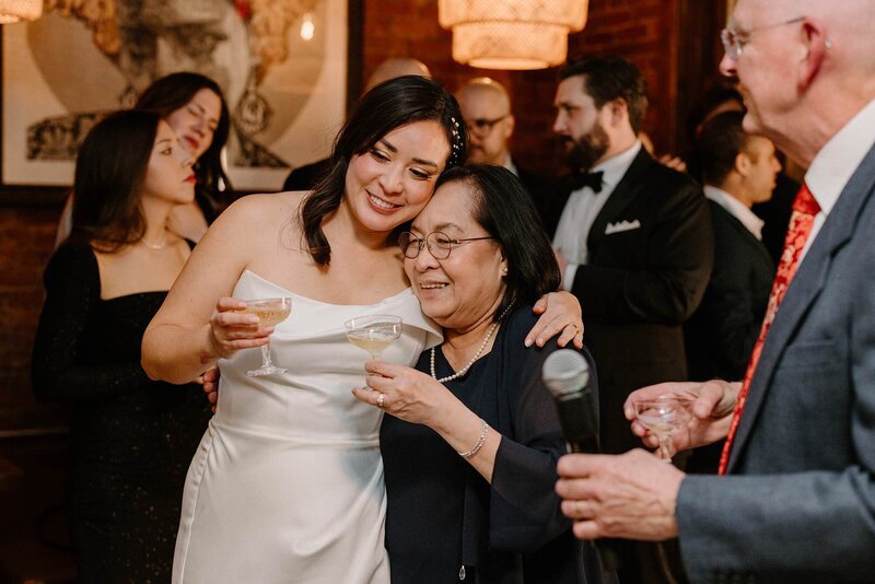 A newlywed hugging a relative as they both hold champagne glasses 