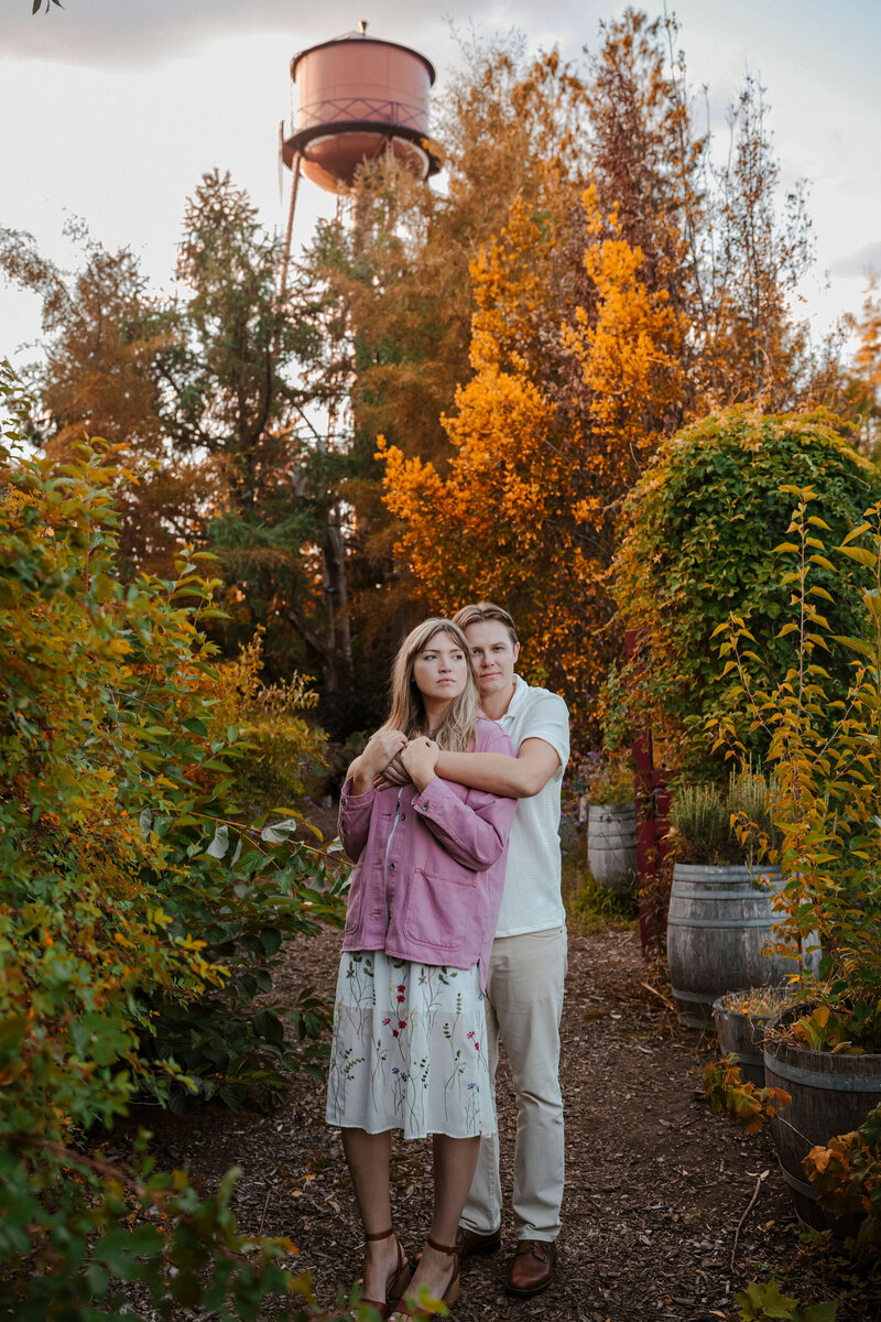 a young engaged couple embracing while surrounded by fall trees
