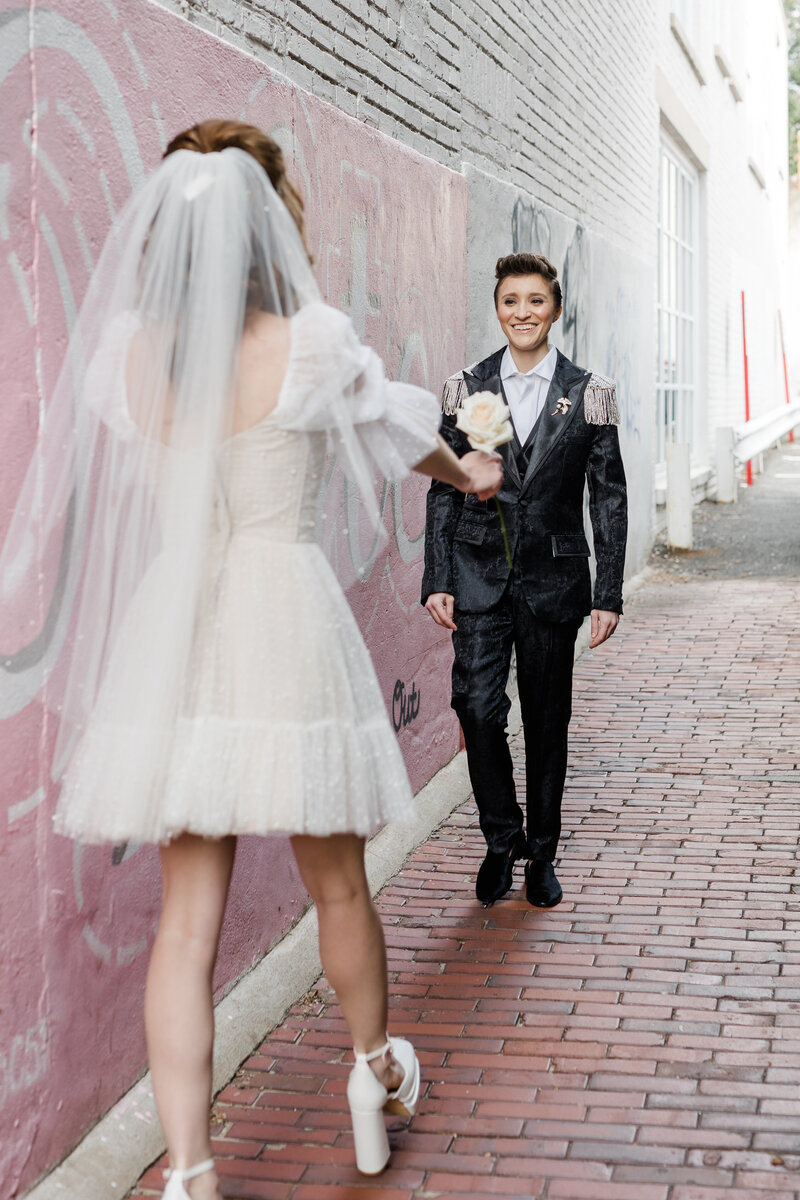 nonbinary wedding couple walking towards on another during first look in alley way with a graffiti wall in Georgetown DC 