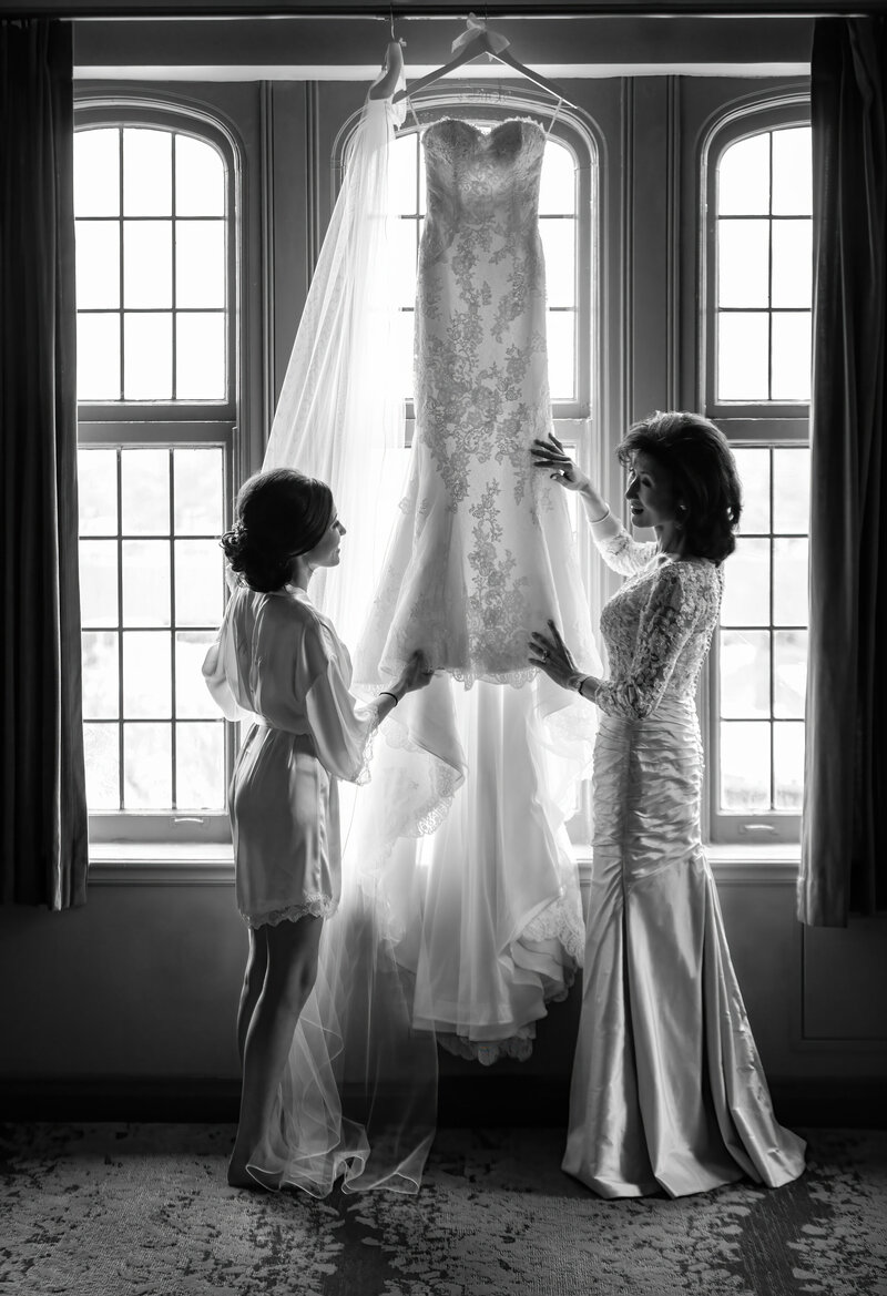 The bride and mother look at each other as the dress hangs in the window.