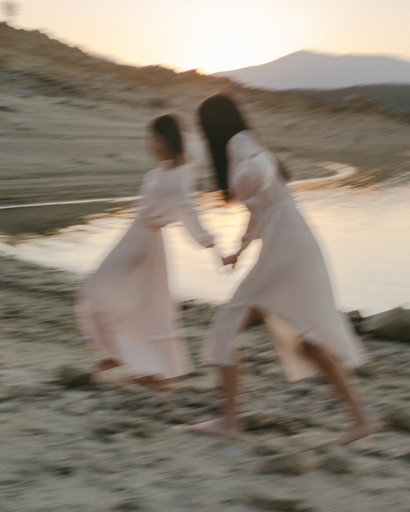 Two boho woman running on the beach holding hands