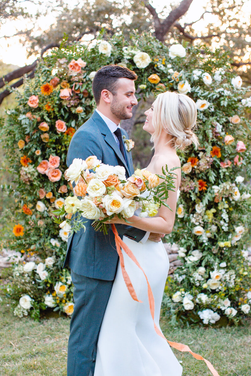 Bride and groom pose in front of an orange floral arch at the wayback in texas