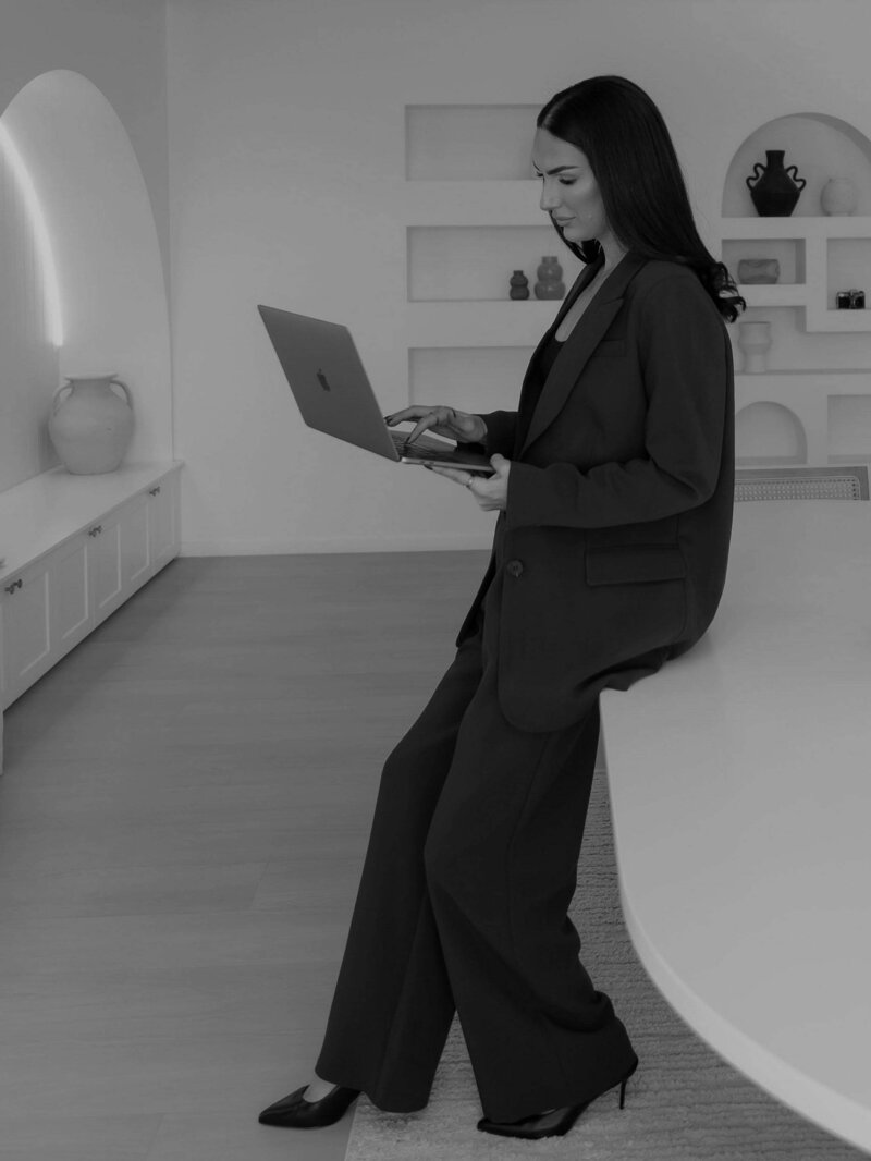 Woman in a tailored blazer working on a laptop while seated on a bench, representing high-end, intentional web design and creative direction.