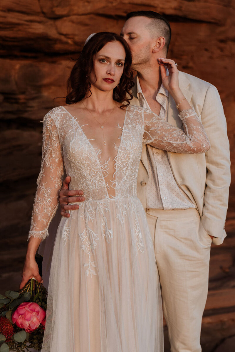 bride and groom embracing in front of a large walk wall in the desert