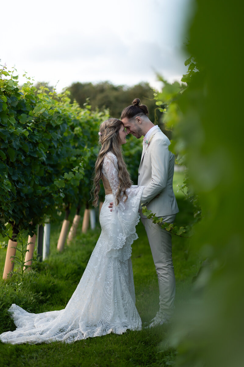 bride and groom in a vineyard with their heads resting against each other