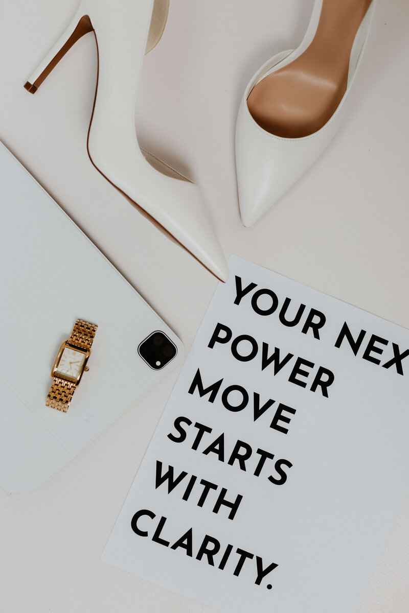 Flat lay featuring white high heels, gold watch, tablet, and a motivational quote reading “Your next power move starts with clarity”—a visual reflection of confident, empowered entrepreneurship.