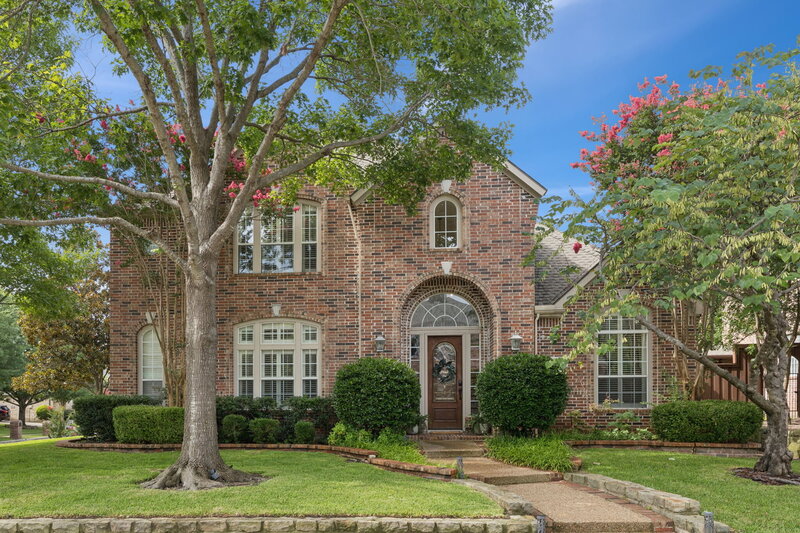Stunning curb appeal at 502 Yaupon Drive with classic brick exterior, arched windows, mature trees, and lush landscaping on a spacious corner lot.