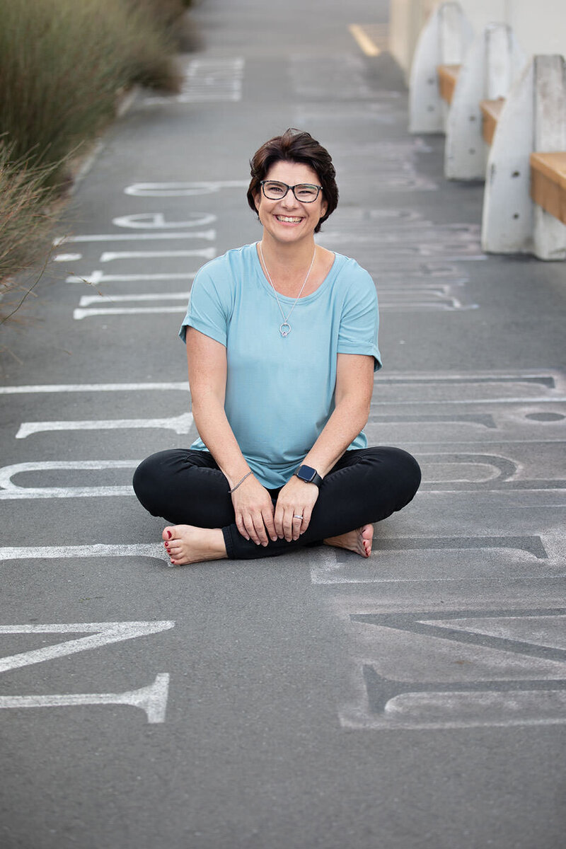 Photographer posing casually sitting on footpath with graffiti in Christchurch city